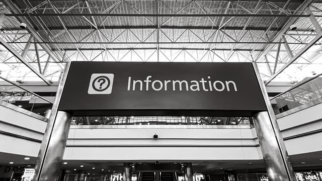Black and white image of an information desk sign in a public place. 