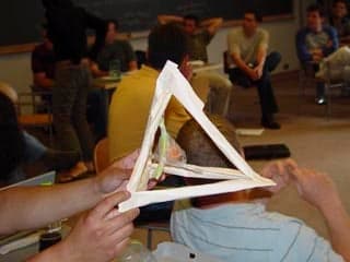A photograph of a student-constructed egg protection device. The device consists of a paper pyramid with an egg suspended within.
