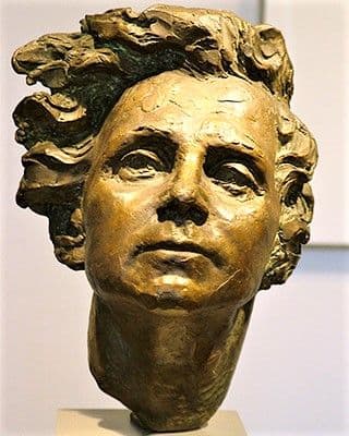 A bronze bust of a woman with strong features and wavy hair.